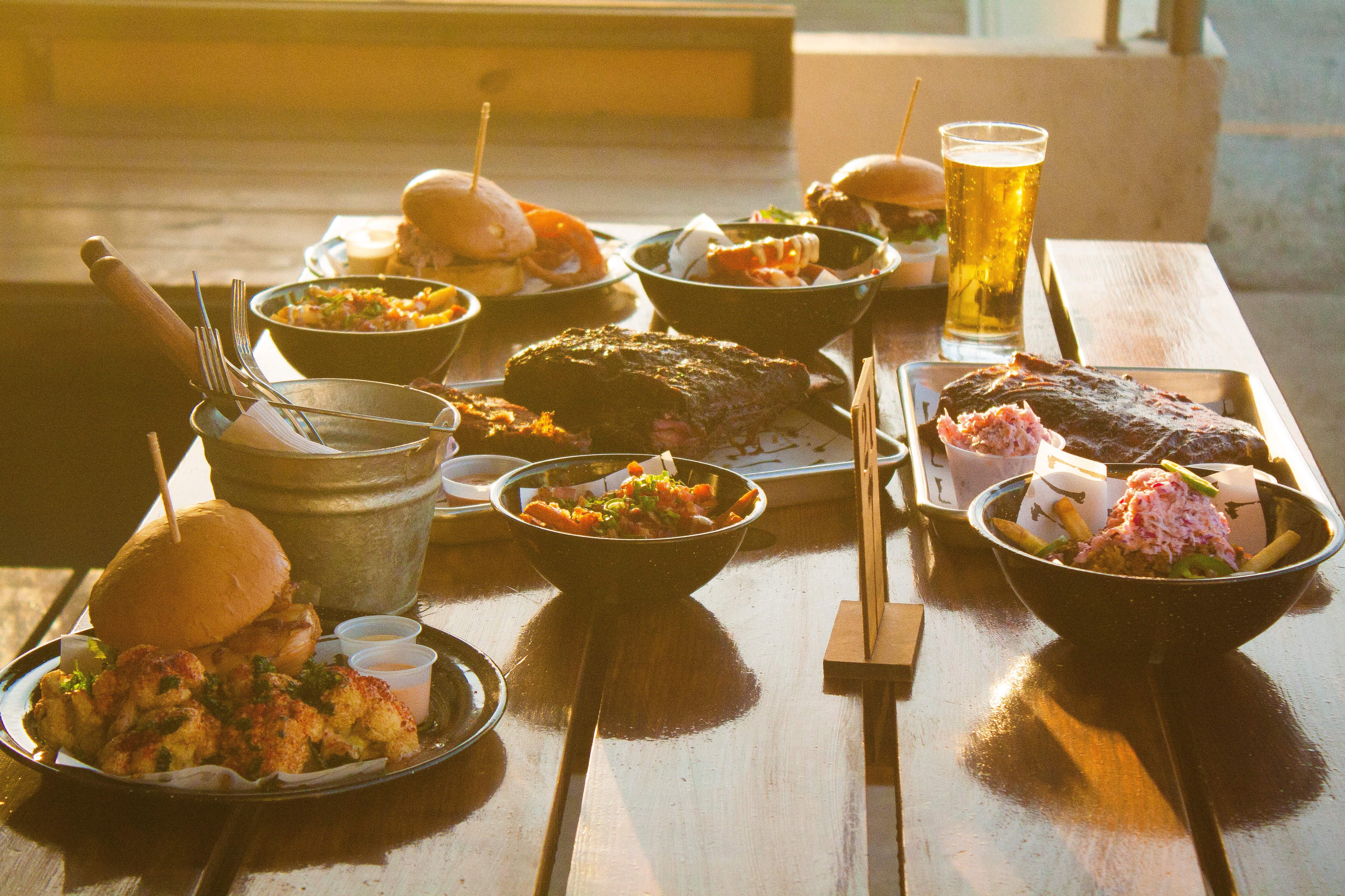 plates of food with burgers, sandwiches, ribs, potatoes, onion rings, and beer.